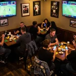 Kèo nhà cái hôm nay features friends engaged in dynamic sports betting while cheering for their teams in a lively sports bar atmosphere